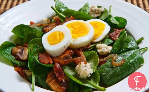 Spinatsalat mit Speck, karamellisierten Zwiebeln, Champignons und Blauschimmelkäse in einer Speckpfanne Sauce Dressing mit einem hart gekochten Ei gekrönt