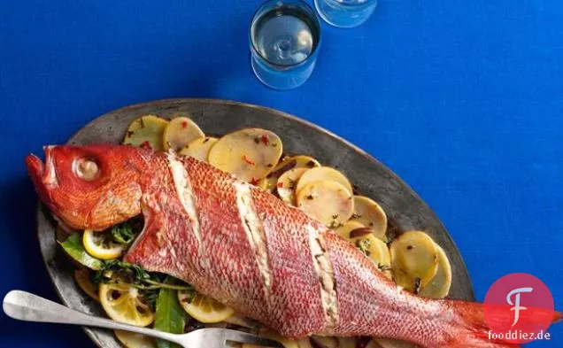Ganzer gebratener Fisch mit geschnittenen Kartoffeln, Oliven und Kräutern
